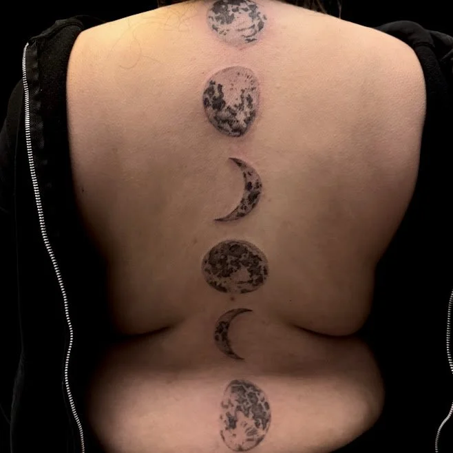 Tattoo on person's back depicting the phases of the moon in black ink.