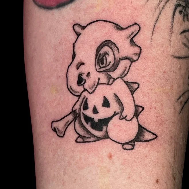Tattoo of a cartoon-style dinosaur holding a carved pumpkin with a spooky face, on skin.