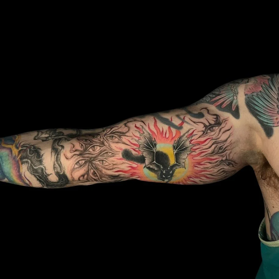 Tattoo sleeve on a person's arm featuring a black panther face with wings and flames, surrounded by multiple eye motifs.