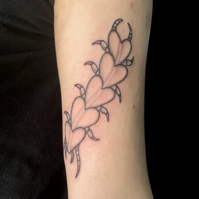 Tattoo of four interconnected pink hearts with angel wings and striped tails on a person's forearm.