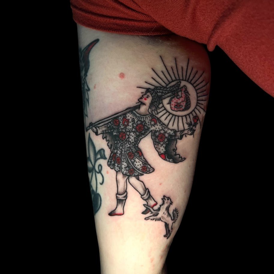 Tattoo of a woman in a patterned dress with flowers, holding a sword and a circular object emitting radiant lines, with a small dog at her feet.
