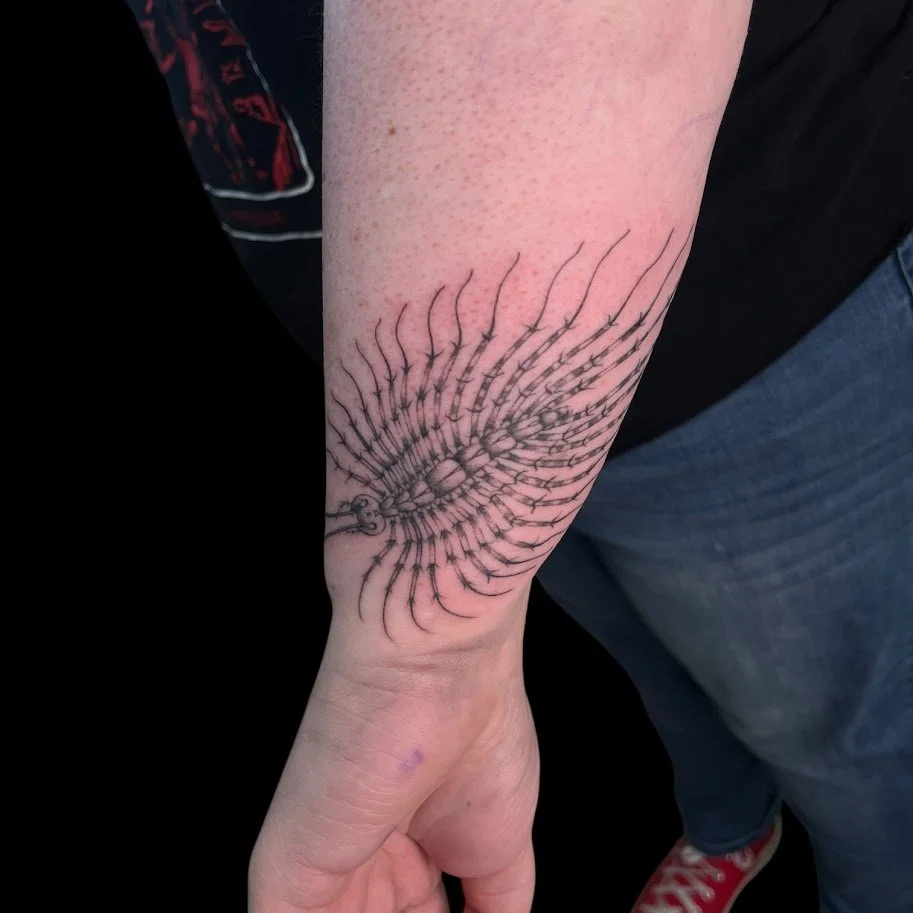 Tattoo of a stylized, abstract sea creature or marine organism on person's forearm.