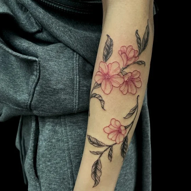 Tattoo of pink flowers and gray leaves on a person's forearm.