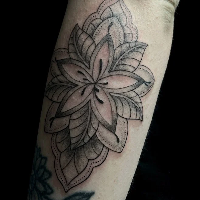 A fresh black and gray outline of a butterfly tattoo on skin, with decorative elements around it.