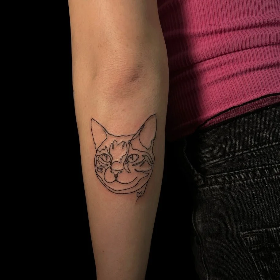 Line art tattoo of a cat's face on a person's arm.