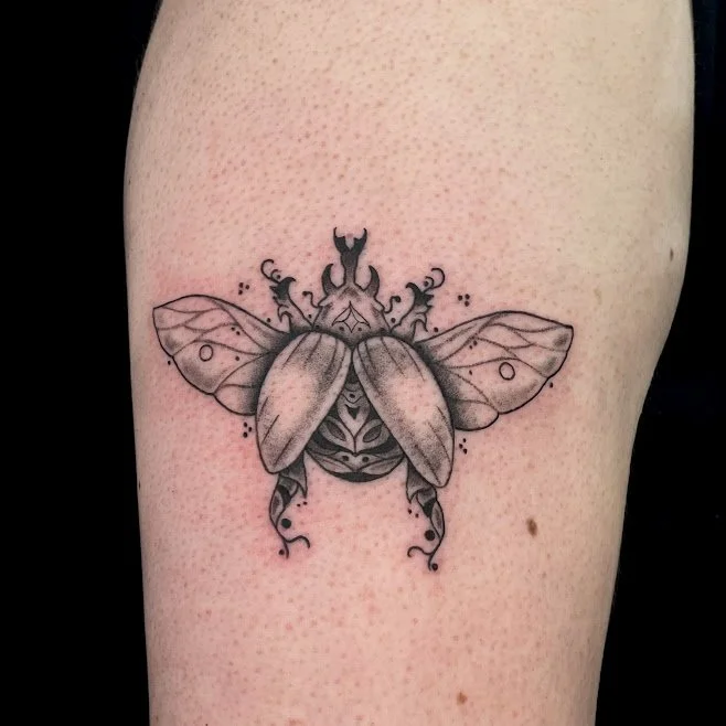Black and gray tattoo of a bee with decorative patterns on its body and wings on a person's skin.
