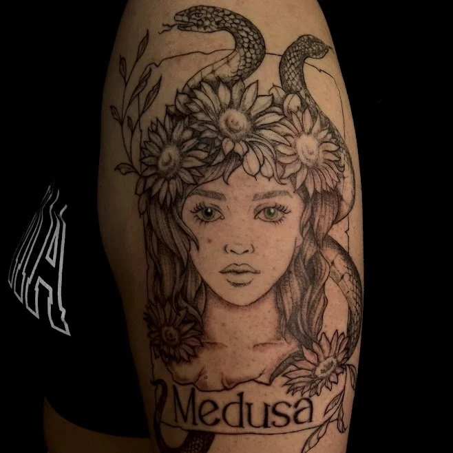 Tattoo of a woman's face with sunflowers in her hair, surrounded by a snake and a branch of leaves, with the word "Medusa" below.