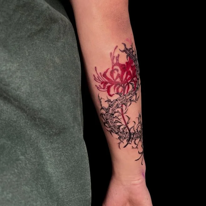 Tattoo of a red and black floral design on a person's forearm.