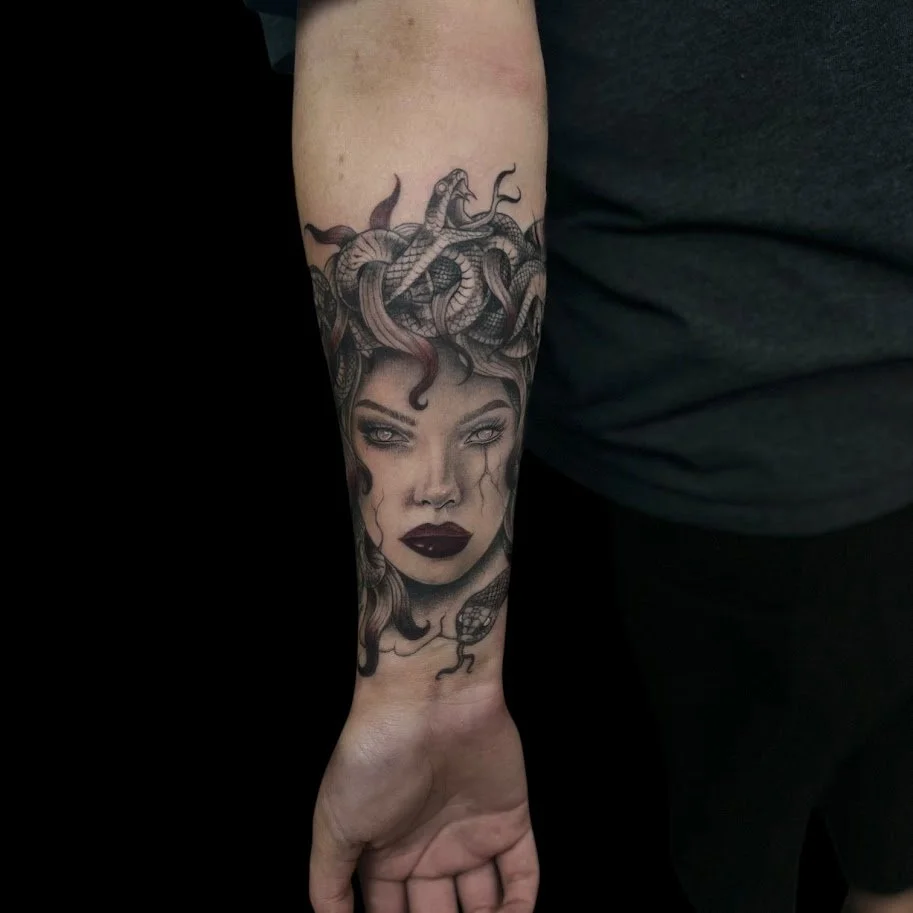 Tattoo of a woman's face with dark lipstick and wavy hair, topped with a snake and several snakes in her hair.