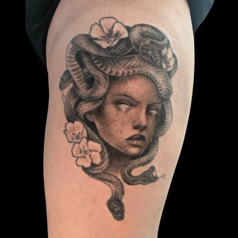 A tattoo of a woman with tears on her face, surrounded by snakes and flowers.