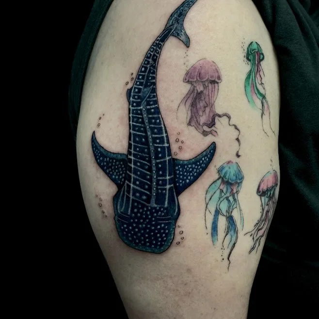 Tattoo of a whale shark and several jellyfish on a person's upper arm.