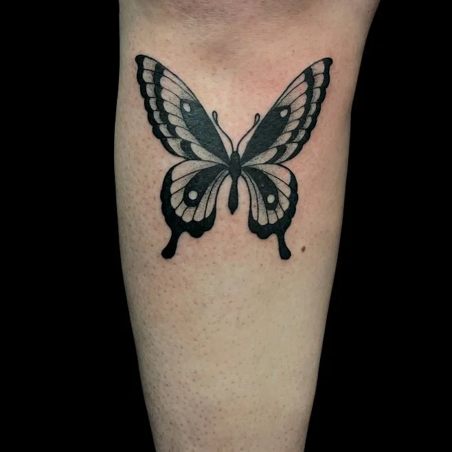 Black and gray butterfly tattoo on person's arm.