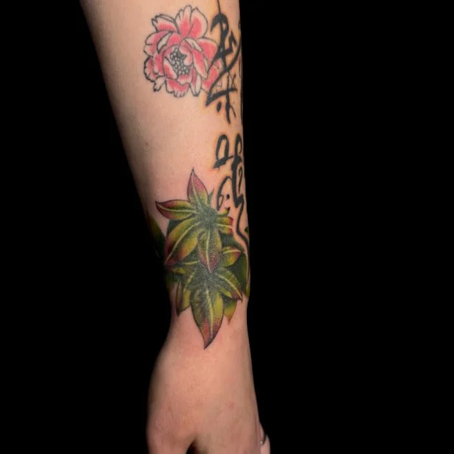 Close-up of a person's forearm with a tattoo of greenish-yellow leaves, partially visible.