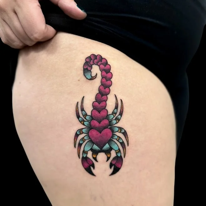 Colorful tattoo of a scorpion with a heart-shaped body and tail on a person's thigh.