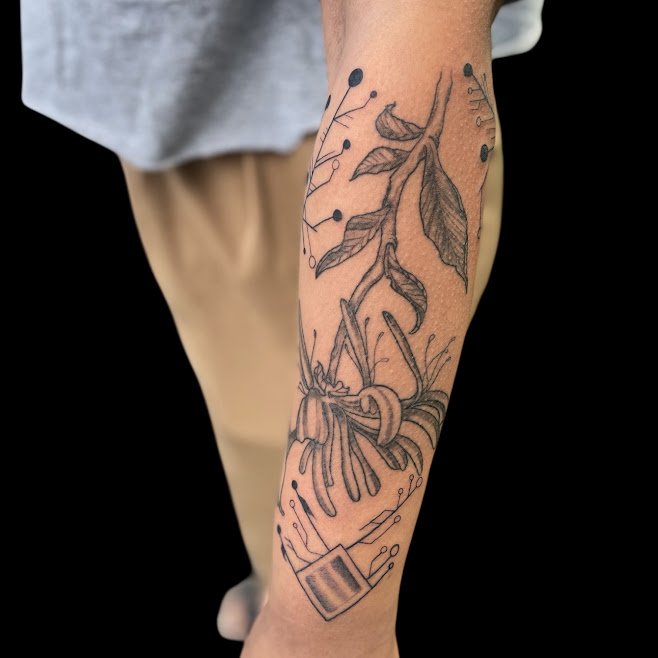 Black and gray tattoo of a lily flower, leaves, and abstract dotted lines on a person's calf.
