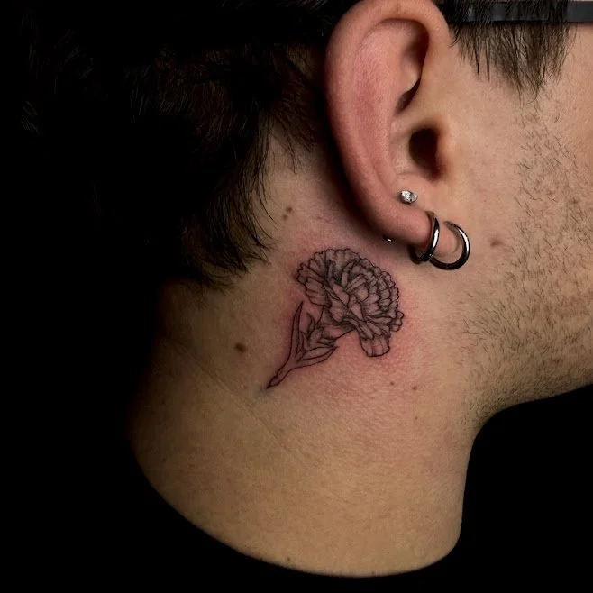 A person's neck with a floral tattoo, multiple earrings, and short dark hair.