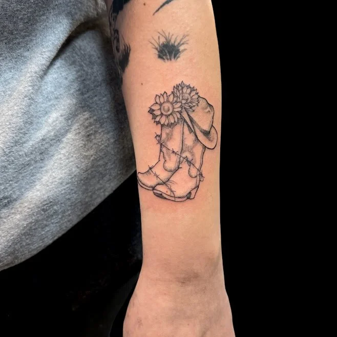 Line art tattoo of a person with flowers as hair, sitting with head bowed and arms crossed, on a person's arm.