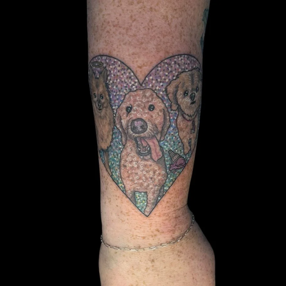 Colorful tattoo of three dogs inside a heart outline on someone’s arm.