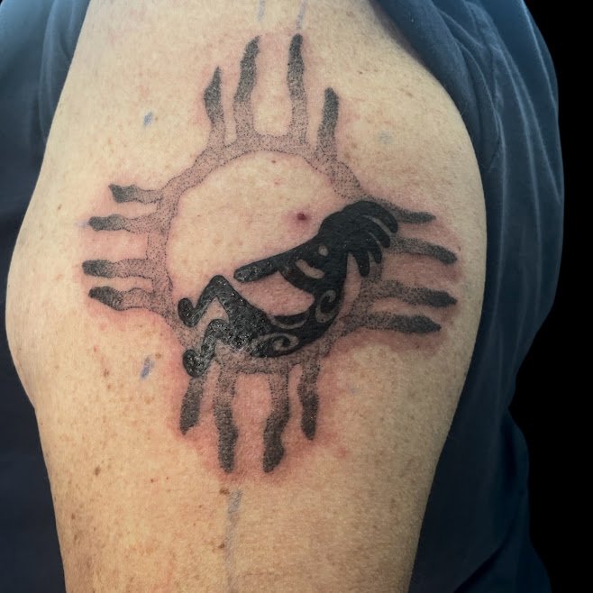 Tattoo of a black whale on a tribal sun design on person's upper arm.