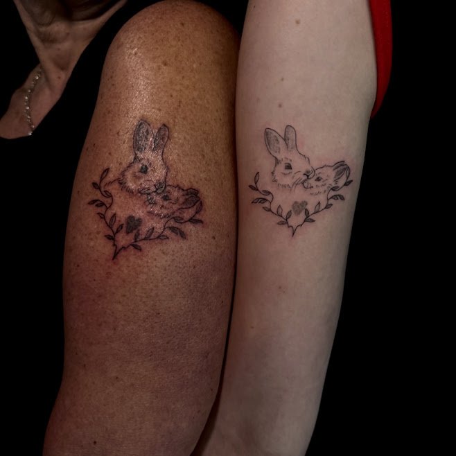 Two people display matching tattooed rabbits with leaves and hearts on their upper arms.