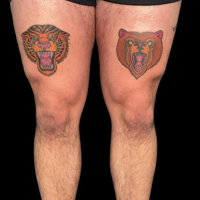 Two tattoos of fierce animal faces on a person's thighs, a tiger on the left and a bear on the right.