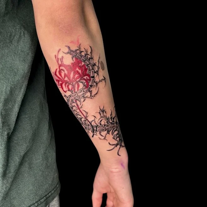 Tattoo of a red spider and a black, tribal-style chain on a person's forearm.