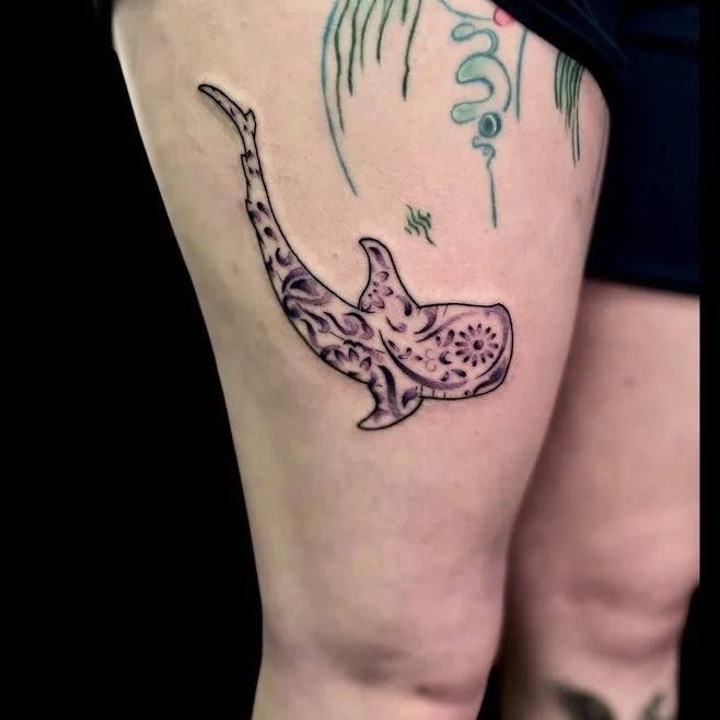Tattoo of a whale with floral and abstract patterns on a person's thigh.