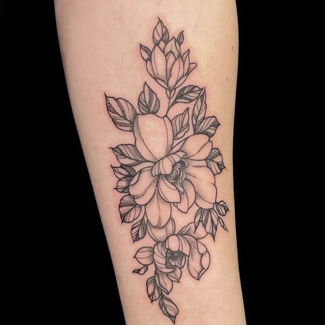 Black outline floral tattoo on a person's forearm, featuring large blooming flowers and leaves.