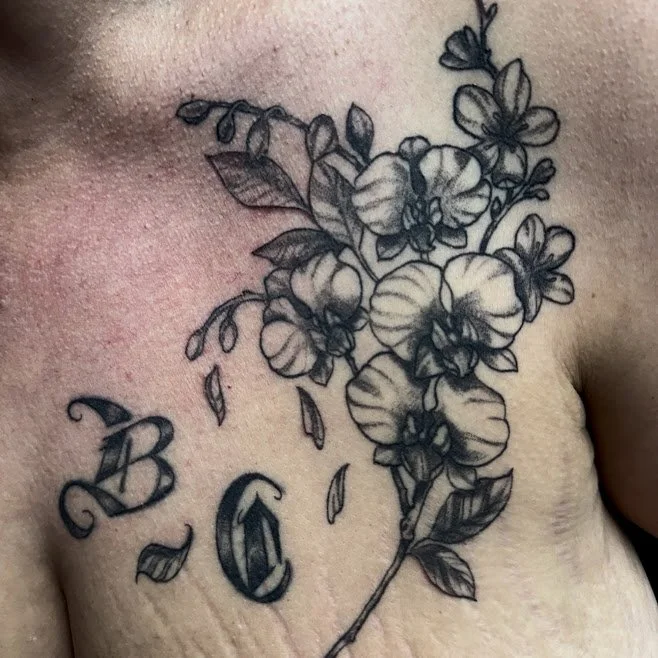 Black and gray tattoo of a floral design with pansies, leaves, and the initials B G on chest.