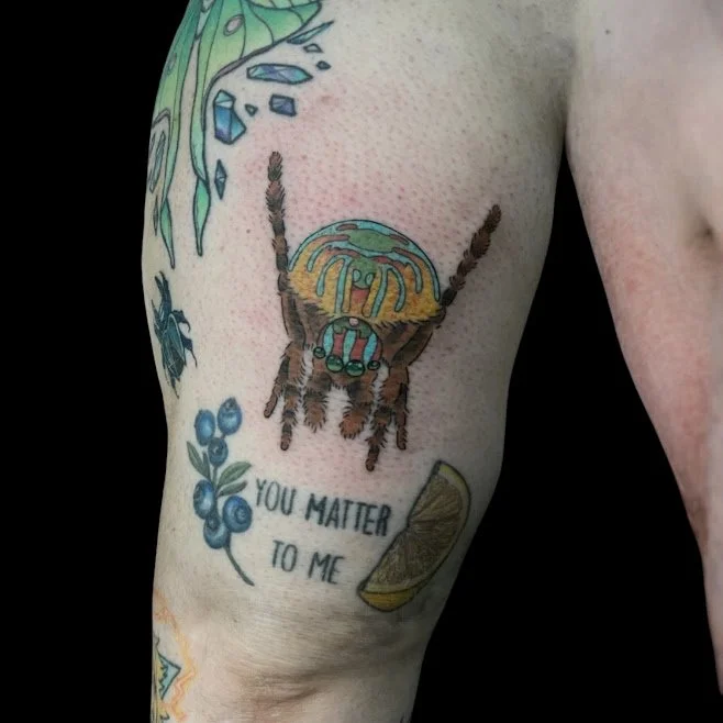 Tattoo of a colorful bee with a quote that says 'You matter to me,' decorated with small blueberries and a lemon wedge.