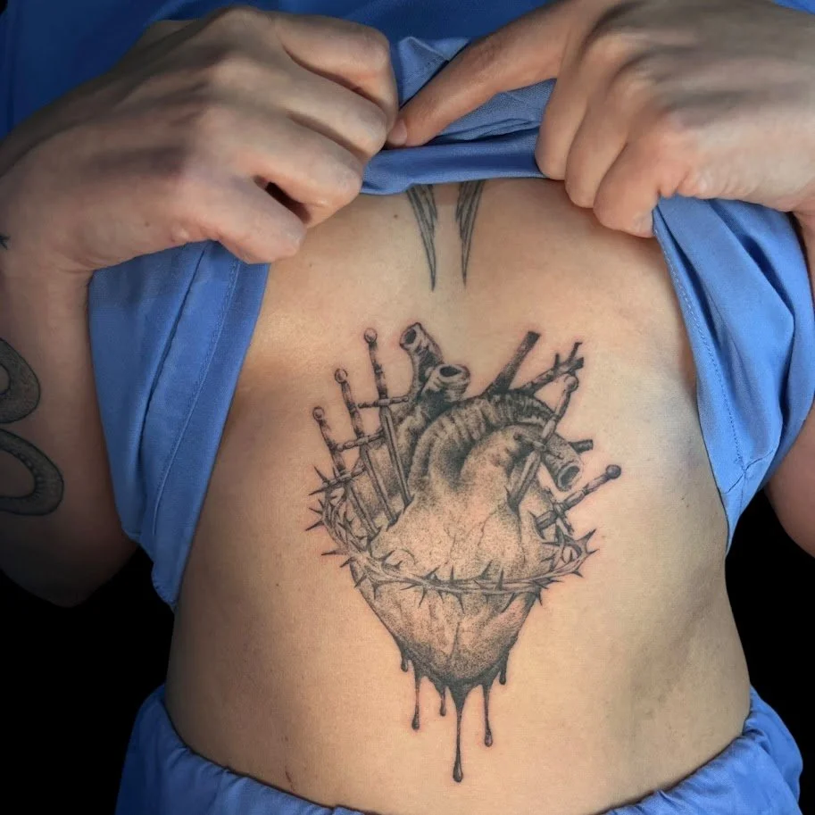 A tattoo of a realistic human heart with multiple surgical pins and needles stuck into it, located on a person's chest.