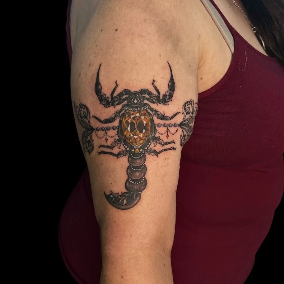 Tattoo of a black scorpion with gold accents on the back of a person's upper arm.