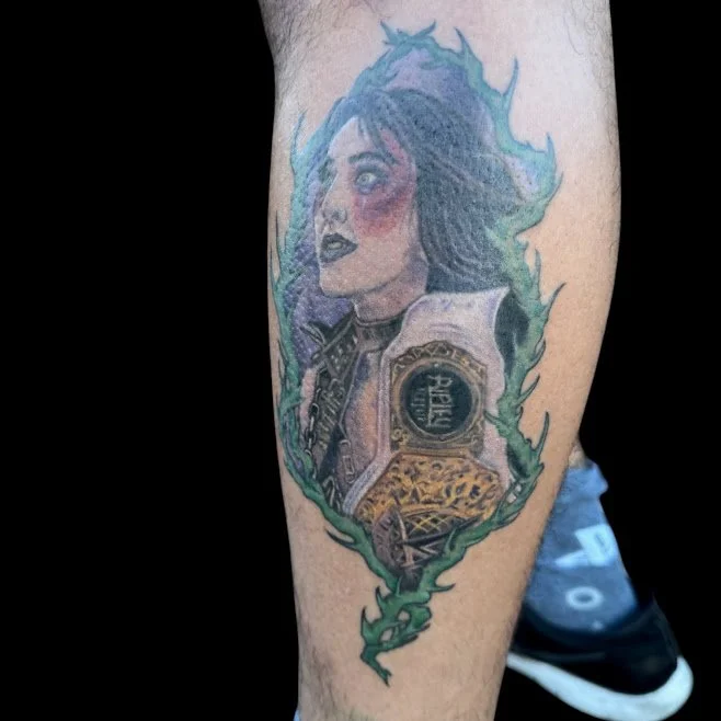 Colorful tattoo of a woman with dark hair, partly covered by a white jacket, surrounded by green smoke or flames, on a person's leg.