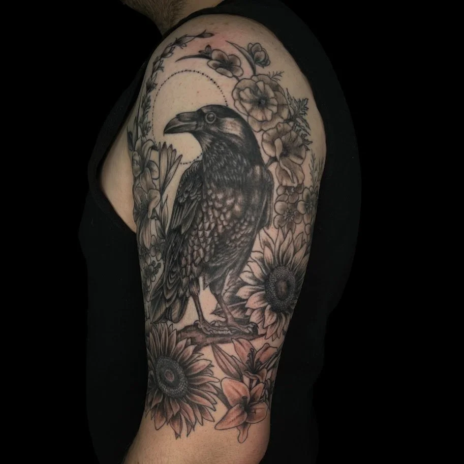 Black and gray tattoo of a raven surrounded by flowers on a person's upper arm.