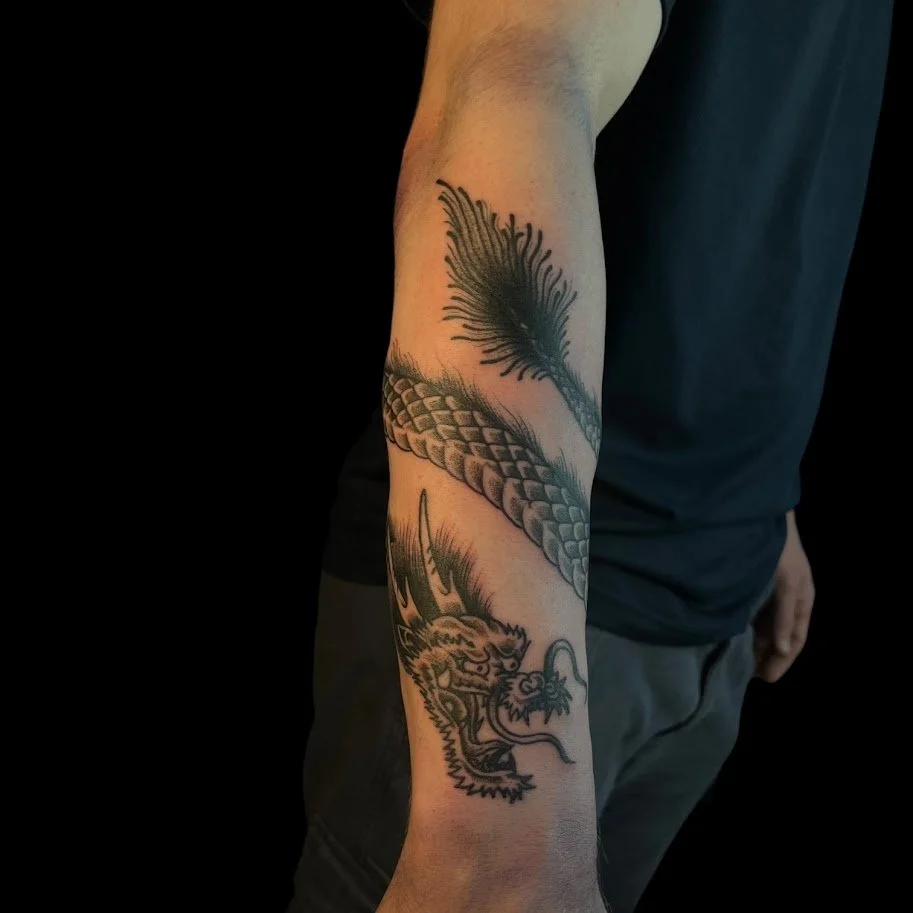 Tattoo of a dragon's head with sharp teeth and whiskers on a person's forearm.