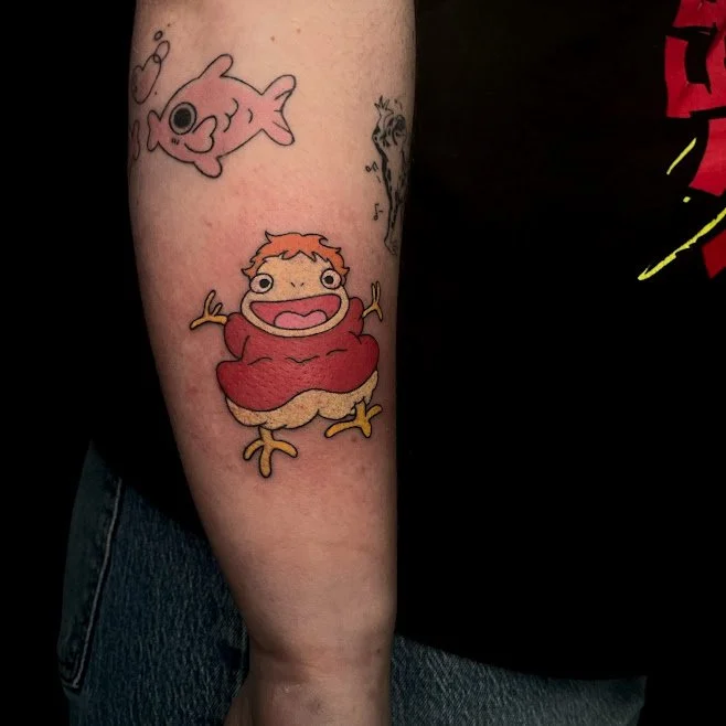 Tattoo on person's arm of a cartoonish chicken character with orange hair, red body, yellow wings, and yellow legs.
