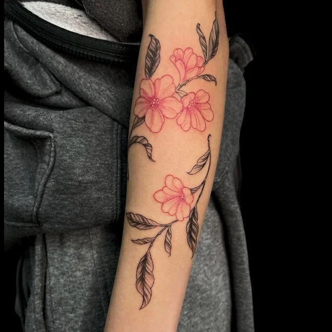 A person's forearm with a floral tattoo design of pink flowers and black leaves.