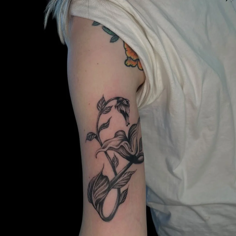 Black and gray tattoo of a flower with leaves on a person's upper arm.