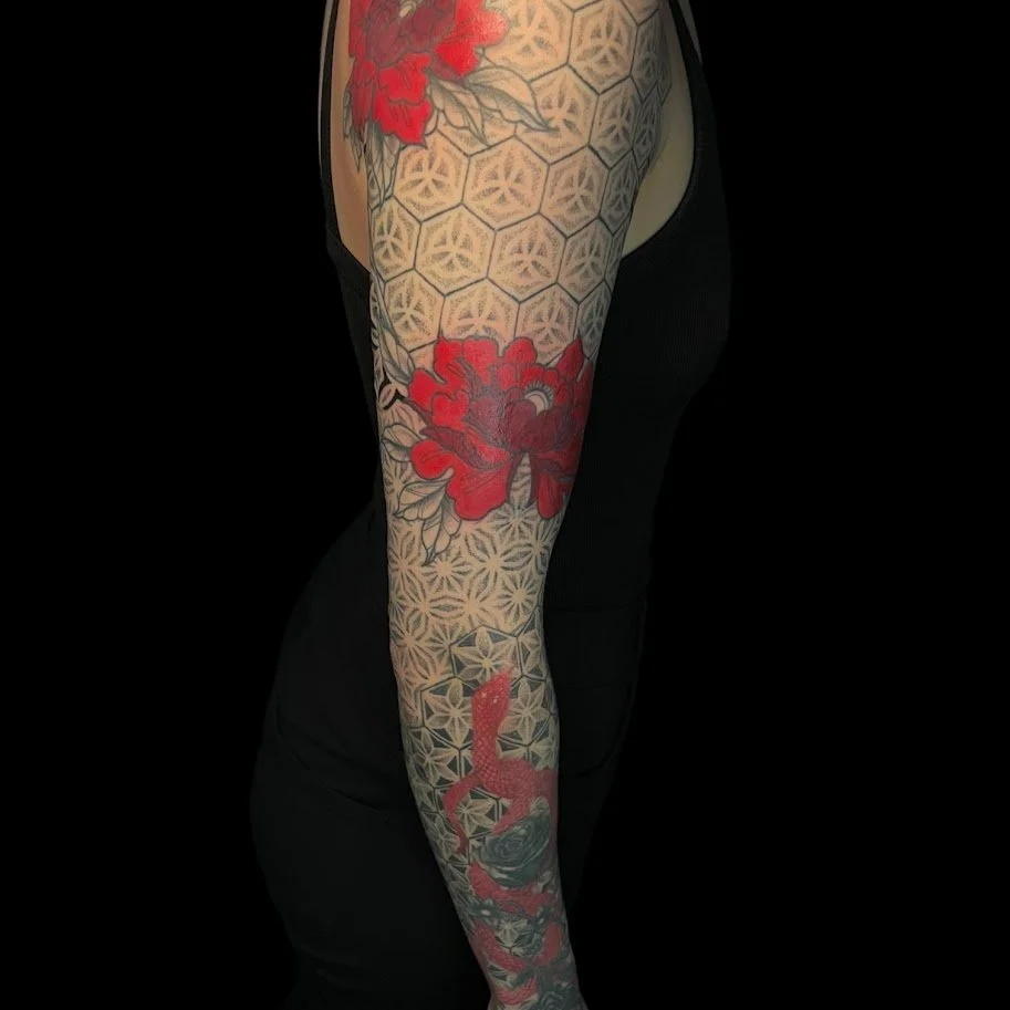A person with a full arm tattoo featuring red flowers, geometric patterns, and a stylized animal head.