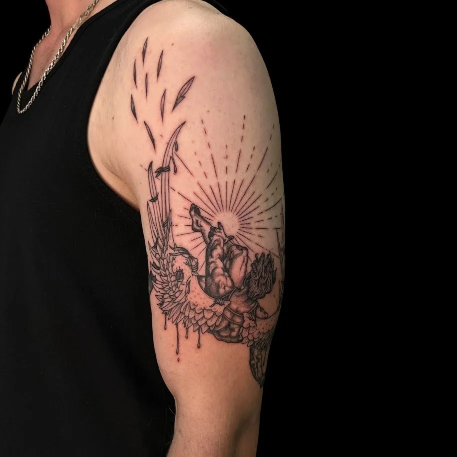 Black and gray tattoo on upper arm depicting a mythological scene with a winged figure, possibly a angel, holding an arrow and a bow, surrounded by a radiant sun and falling feathers.