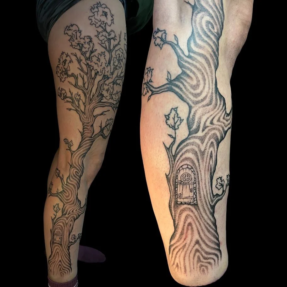 Tattooed legs of two people, each with a large tree design that includes a door at the base of the tree trunk. The trees have detailed bark and branches, with a few leaves on the branches. The tattoos are in black ink with shading to add depth.