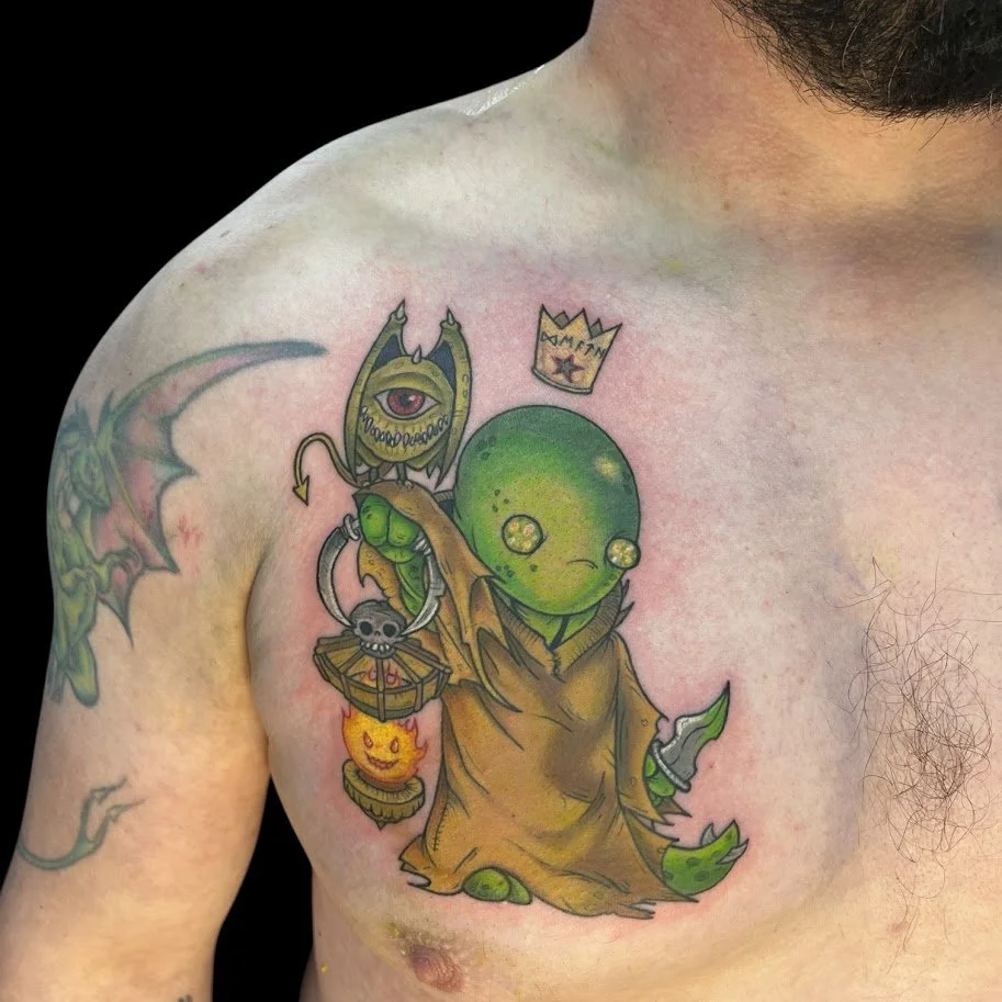 Tattoo of a green, cartoonish creature with a large head, small limbs, and dressed in a brown robe, holding a dagger in one hand and a lantern with a smiling face in the other, on a man's chest.