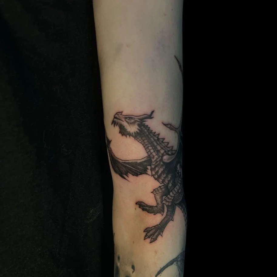 Black and gray dragon tattoo on person's forearm.