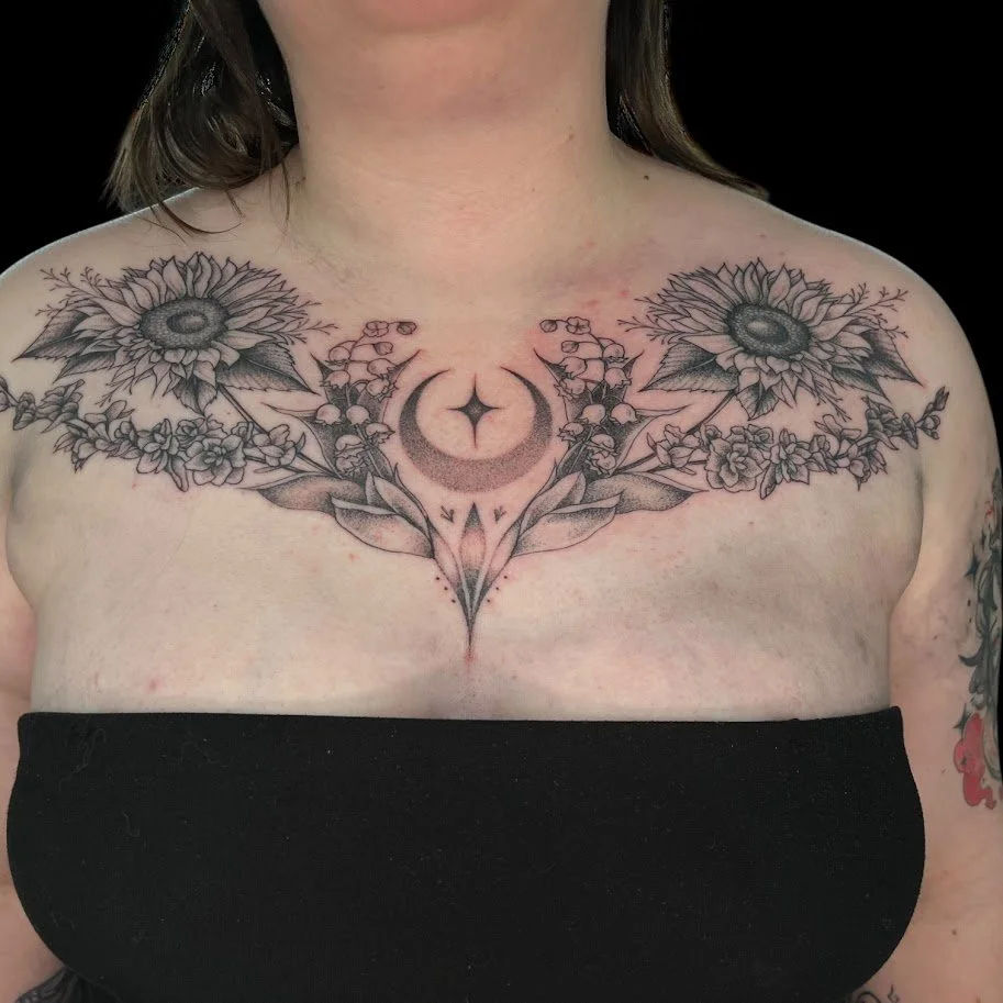 Black and gray tattoo featuring sunflowers, a crescent moon with a star, and floral designs across the upper chest and shoulders.
