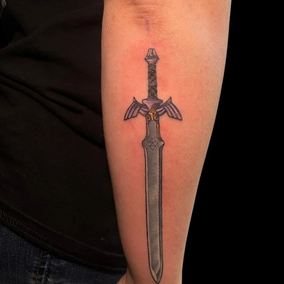 A tattoo of a sword on a person's forearm. The sword has a detailed blade, a dark handle, and small wings near the hilt.