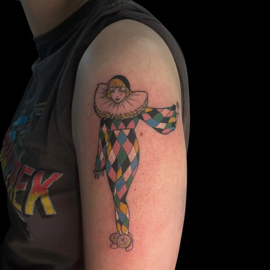 Tattoo of a clown with a ruffled collar and harlequin patterned pants on a person's upper arm.