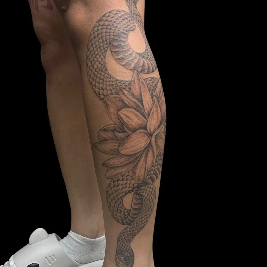Tattoo of a snake intertwined with a large flower on a person's leg.
