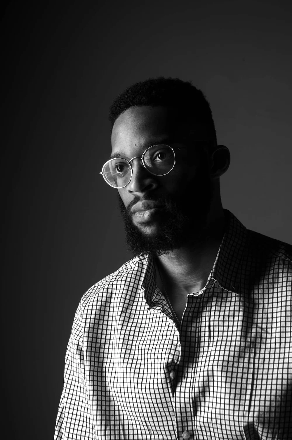 Black and white portrait of a man wearing glasses and a checkered shirt, looking slightly to the side.