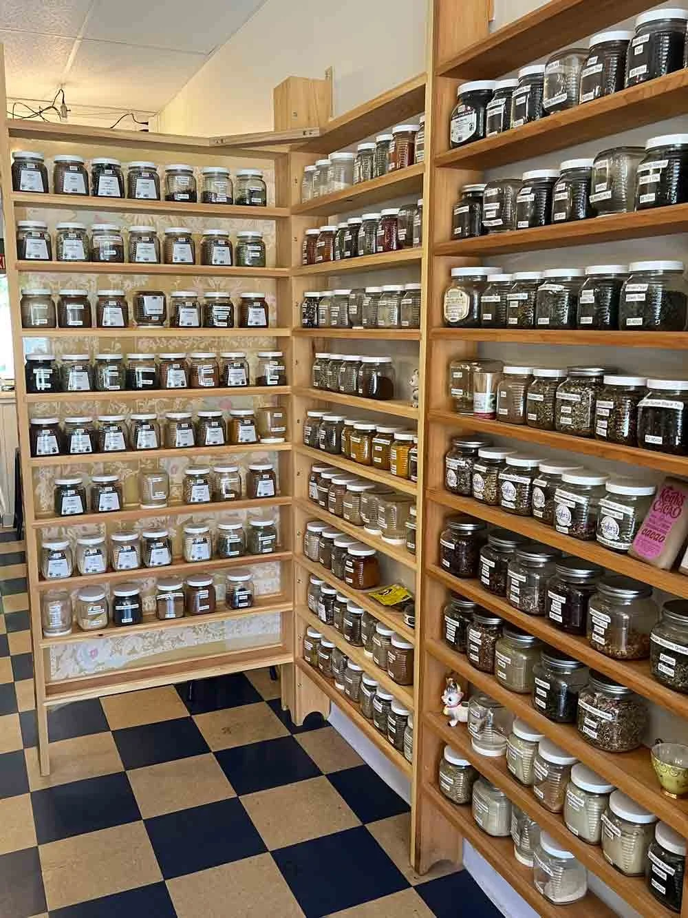 Wooden shelves filled with labeled jars of various spices and herbs in a store or kitchen.