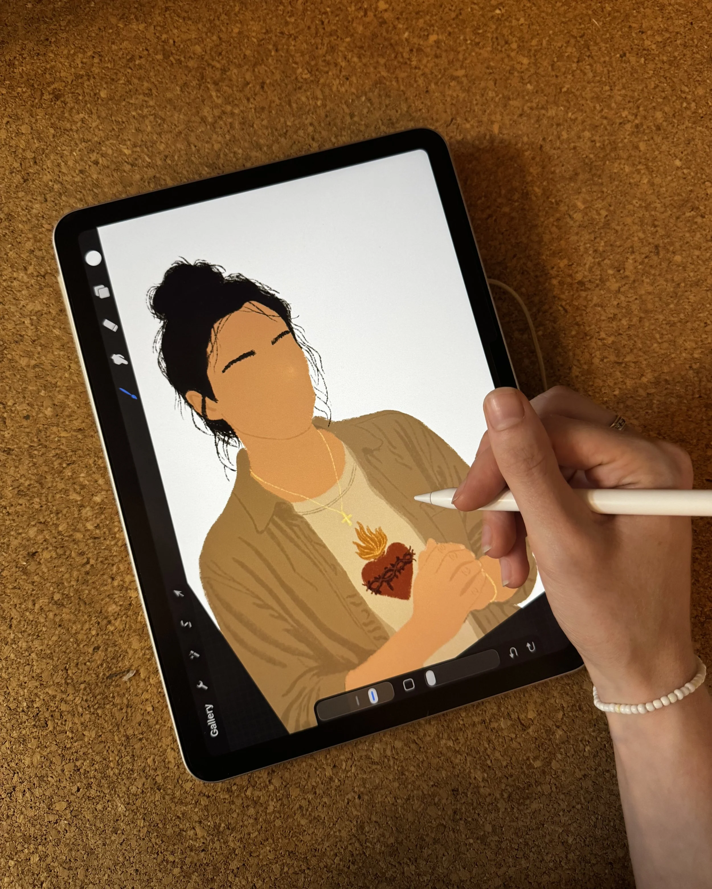 A person holding a stylus drawing a digital portrait of a woman with dark hair styled in a bun, wearing a necklace with a cross, on a tablet with a cork-textured surface in the background.